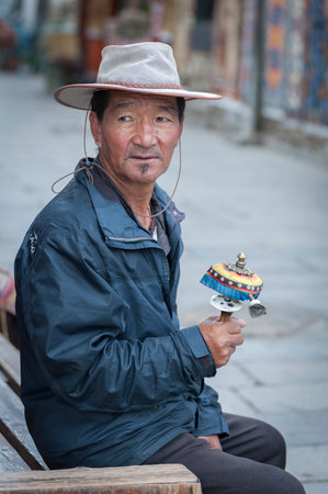 LHASA, TIBET, CHINA - AUGUST, 17 2018: Unidentified Tibetan man in traditional clothes sit on a bench nearby Jokhang temple praying with prayer wheelsのeditorial素材