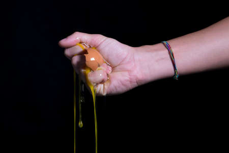 Yolk falling down on a black background, holded by a handの写真素材