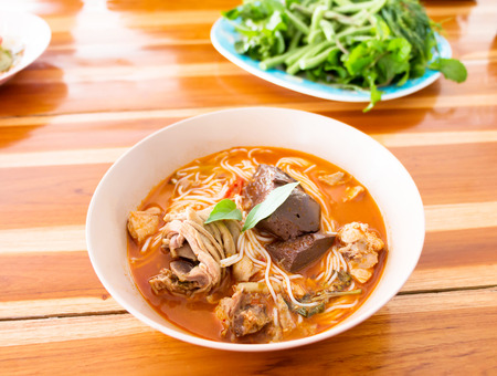 a bowl of spicy noodles with vegetable on wooden table
