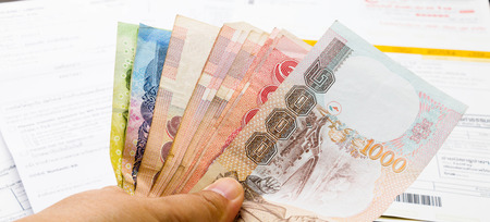 hand holding thai baht cash to pay billsの写真素材