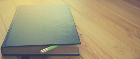 dark blue book with pencil on brown wooden table for background, the blank space on the left for...