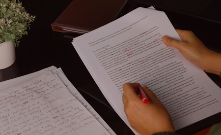 hand holding red pen to correct proofreading paper on black table in officeの写真素材