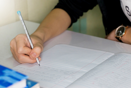 student hand writing English lesson on white table in classroom