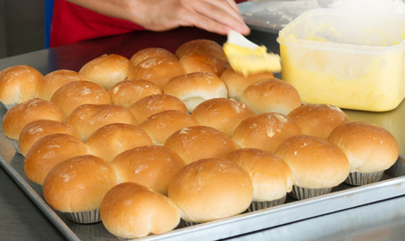 moving hand brushing butter on fresh new baked bread in kitchenの写真素材
