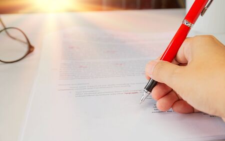 proofreading paper on white table with hand and red pen