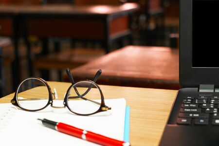 glasses, pen, and computer on teacher's table in classroomの写真素材