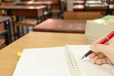 teacher's hand holding red pen checking on student's homework in classroomの写真素材