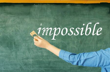 hand erasing prefix of impossible on chalkboard in classroomの写真素材