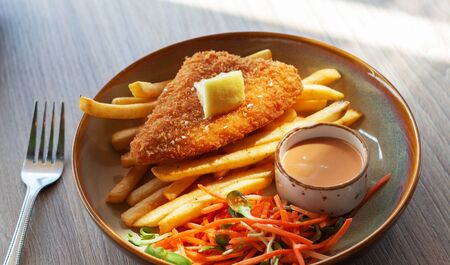 fried fish fellet wiht french fries and veggies on plate in restaurant