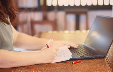 woman's hand holding pen marking on proofreading paper with laptop on desk in office の写真素材