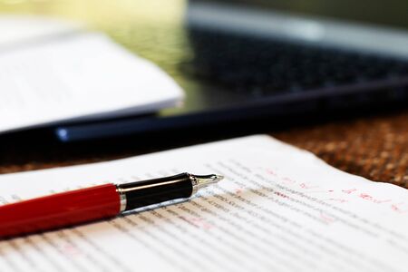 close up pen on proofreading paper on desk with laptop in office