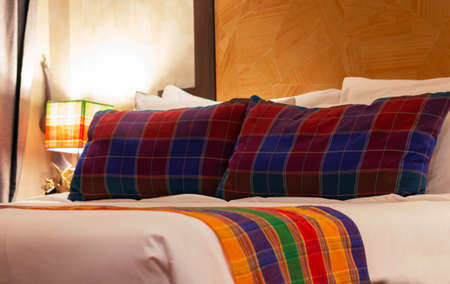 colorful pillows in bed with lamp on bedside table at night