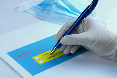 hand wearing medical gloves holding pen to check on Covid-19 test result with mask on table