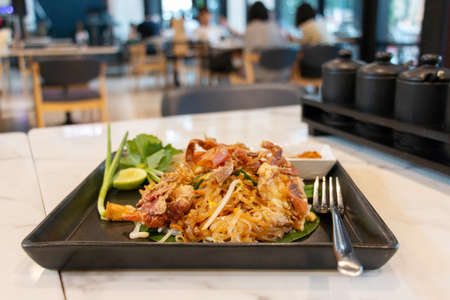 crispy crabs pad thai in black plate on white table in restaurant with blurred customersの写真素材