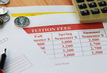 close up paper of school tuition fees on wooden table with coins, red pen, and calculatorの写真素材