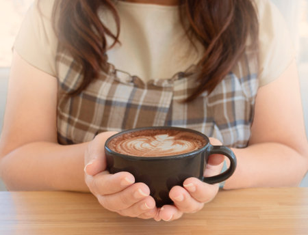 hand holding hot organic cocoa with foam froth art in black ceramic cup