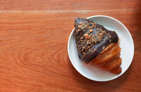 top view of chocolate coated croissant on white plate on wooden table with copy space