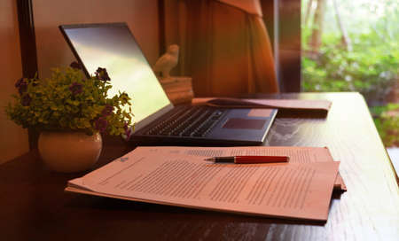 red pen over blurred paperwork on wooden table with laptopの写真素材