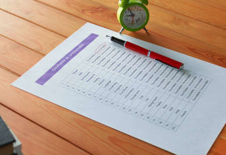 English grammar test sheet with red pen and clock on wooden table in classroom