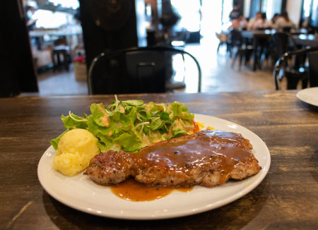 fresh juicy pork steak with gravy sauce and vegetable on white plate in restaurantの写真素材