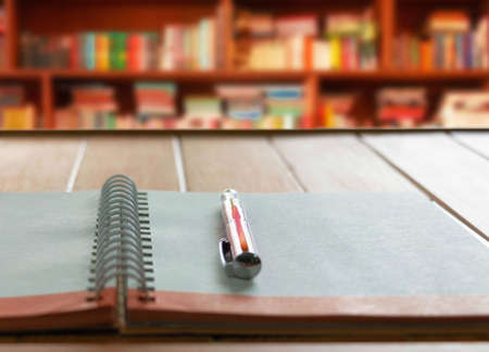 pen on notebook with white loop on wooden table with blurred bookshelf backgroundの写真素材