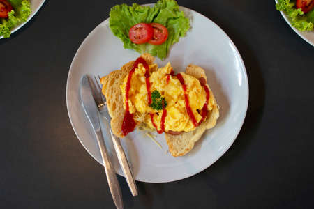 fresh yellow scrambled egg on bread on white plate with vegetable for breakfastの写真素材