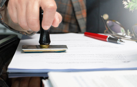 hand holding rubber stamper on white paperwork in officeの写真素材