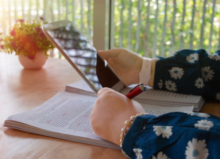 hand holding red pen over blurred paperwork on wooden table in office for proofreading conceptの写真素材