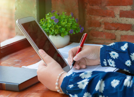 hand holding red pen over blurred paperwork on wooden table in office for proofreading concept