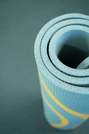 A black yoga and Pilates mat lies on the gym floor on a black background