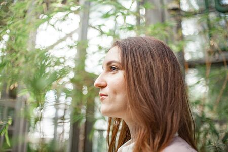 young woman standing in greenhouse and looking straight at camera. Plant parent concept