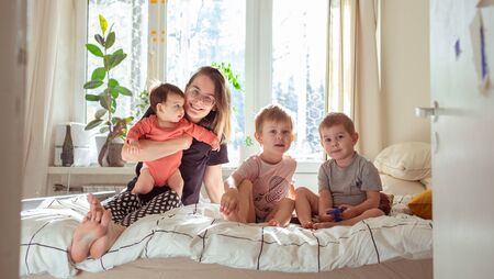 young mother sitting on the bed with her three toddler and infant childrenの写真素材