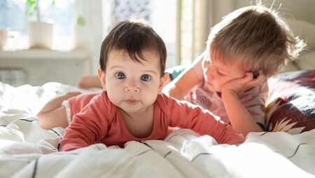 Little cute baby infant lying on the bed together with her toddler brotherの写真素材