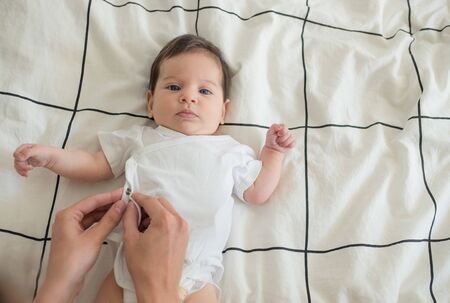 little newborn baby lying on bed with mother hands dressing a babyの写真素材