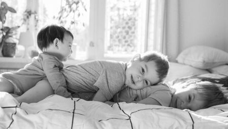 Two toddler brothers and little cute baby sister lying on the bed on each other