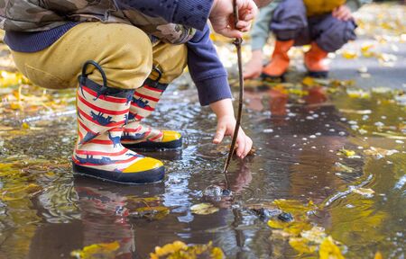kids legs in rubber rain boots in puddle in autumnの写真素材