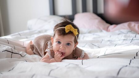 Little infant baby girl portrait lying on bed with yelow bow on headの写真素材
