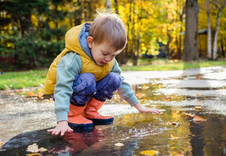 toddler boy sitting in puddle in rubber rain bootsの写真素材