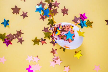 Egg with star shaped colourful confetti on yellow background. Festive bright decorationsの写真素材