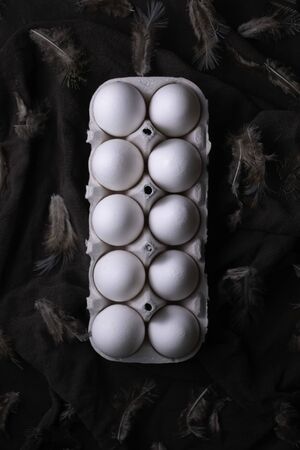 Easter eggs in dark mood concept light on black textile background with bird feather
