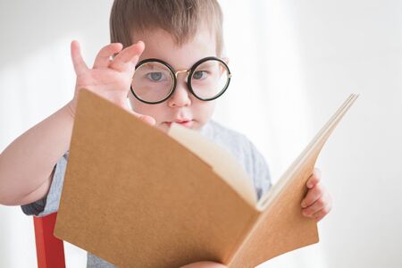 Cute toddler boy reading a book in glasses. Smart preschooler. Back to school conceptの写真素材