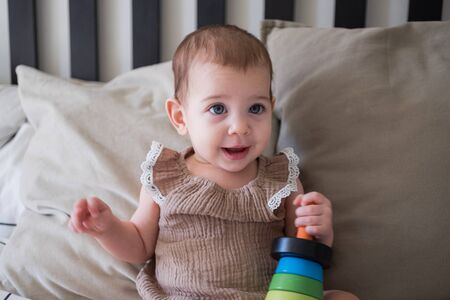 Little infant girl playing with wooden pyramid on bed at home
