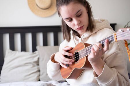 Close up portrait of young woman playing ukulele guitar at home. Spending time at home...