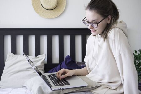 Woman making video call via laptop sitting on bed at home. Lifestyle concept. Social distance self...