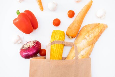 Grocery food delivery at home flat lay on white background. Paper craft bag with grocery and various vegetables top view. Stay home, keep social distance, contact less deliveryの写真素材