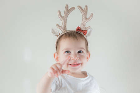 Little infant girl with shiny glitter rain deer horns costume. New year and christmas party...