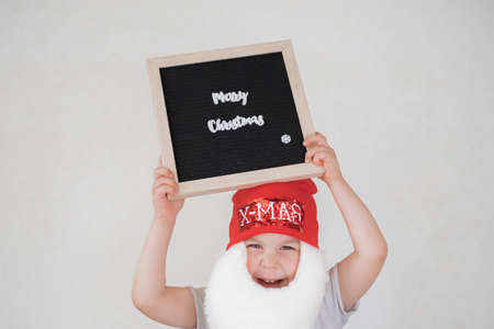 toddler boy in Santa Claus costume with beard and red hat on white backgroundの写真素材