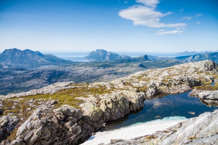 A small lake with snow and view towards mountains and the sea in Northern Norwayの写真素材