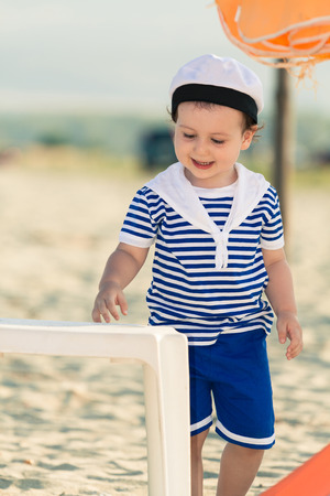 Close up of sweet toddler dressed as a sailor standing on a beach. Photo with untraditional color rendering for artistic lookの写真素材