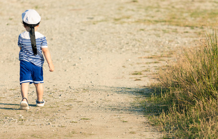Sweet toddler dressed as a sailor walking with determination on a gravel road. Photo with untraditional color rendering for artistic lookの写真素材